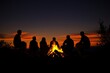 © Guy - Silhouette of A group of people sitting around a fire, with the sun setting in the background
