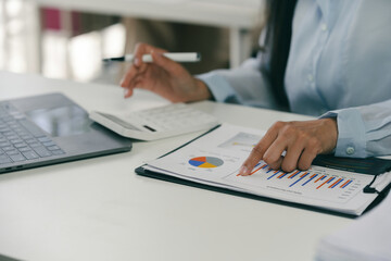 Wall Mural - Businesswoman is analyzing financial charts at her desk, using a calculator to assist with her calculations