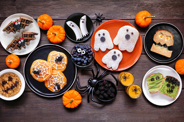 Poster - Spooky Halloween breakfast table scene over a dark wood background. Above view. Variety of pancakes, toast, oatmeal and fruit.