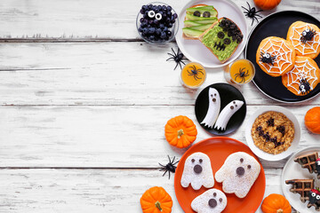 Wall Mural - Spooky Halloween breakfast side border over a white wood background with copy space. Top down view. Assorted pancakes, toast, oatmeal and fruit.