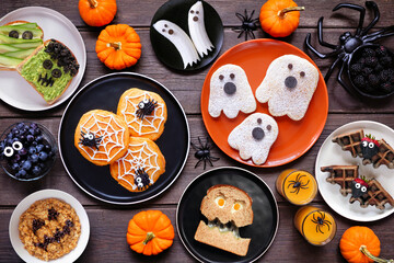 Poster - Spooky Halloween breakfast table scene over a dark wood background. Top down view. Assorted pancakes, toast, oatmeal and fruit.