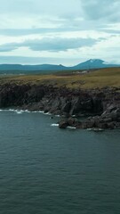 Wall Mural - Top view of landscape with northern mountains and cliffs by sea. Clip. Fantastic landscape of green northern mountains. Cinematic landscape of rocky coast and green mountains on cloudy day