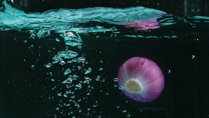 Macro of fresh red onions dropping into water with splash water with separated black background. High-speed photography on black background. Cooking and freshness concept. Design for poster. Pabulum.