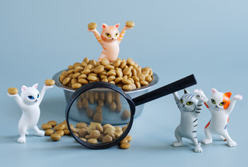 Funny toy kittens near bowl, dry cat food and magnifying glass. Concept of choosing best pet food. Concept of studying nutritional properties of animal food. Toy world