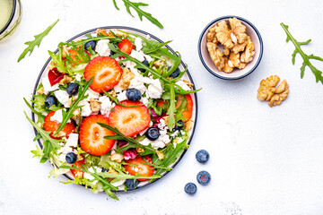 Wall Mural - Strawberry and feta salad with arugula, lettuce, blueberries, cheese and walnuts, white background, top view