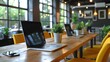 © aicandy - A modern, brightly lit co-working space with large windows, yellow chairs, and a wooden table adorned with laptops and small potted plants, creating an inviting work environment