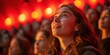 © aicandy - Captivated audience members in a theater filled with warm, ambient lighting, showing a young woman gazing upwards attentively, bathed in a red and orange glow