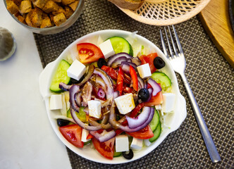 Wall Mural - Traditional Greek salad with fresh vegetables, feta cheese and black olives served on white plate.