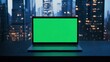 © Aliaksandr Siamko - A laptop with a green screen is sitting on a desk in front of a city skyline