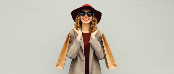 Wall Mural - Autumn portrait of beautiful young woman with shopping bag, stylish girl in coat on gray background