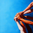 © PTC_KICKCAT - Group of diverse people joining hands in unity against a blue sky background, symbolizing teamwork, strength, and collaboration.