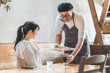 Wall Mural - ランチを食べにカフェ・飲食店に来たアジア人女性と料理を運ぶ配膳する男性店員・スタッフ
