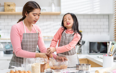 Portrait of enjoy happy love asian family mother and little toddler asian girl daughter child having fun cooking together with dough for homemade bake cookie and cake ingredient on table in kitchen