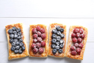 Poster - Tasty puff pastries with berries on white wooden table, flat lay. Space for text