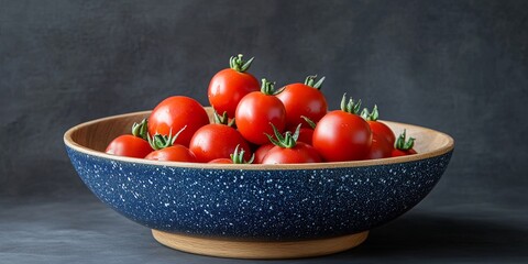 A bowl of red ripe tomatoes with green stems on a dark background.