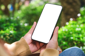 mockup image of a woman holding mobile phone with blank white desktop screen in the outdoors