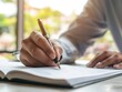© Obsidian - Close up of male hands writing in notebook at table in office.