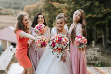 A group of women are posing for a picture with bouquets of flowers. The bride is wearing a white dress and the other bridesmaids are wearing pink dresses. Scene is joyful and celebratory