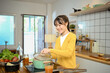 © Prathankarnpap - Happy young woman in a yellow cardigan is enjoying cooking in the kitchen at home