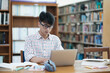 © ijeab - Young Asian male sitting inside a library alone doing research. Man working on a project. Young man doing research for a case.