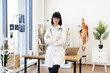 © sofiko14 - Confident female doctor standing with arms crossed in modern medical office. Professional healthcare worker in white lab coat with stethoscope. Contemporary medical equipment and anatomical model.