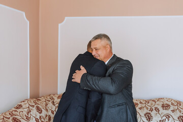 A man and a woman are hugging each other in a room. The man is wearing a suit and tie, and the woman is wearing a dress. Scene is warm and affectionate, as the two people are embracing each other