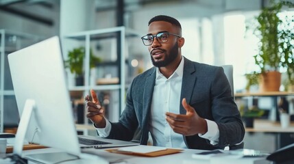 Virtuak business meeting online. A prosperous businessman uses a computer and video chat to negotiate with his multicultural business partners while seated at his desk.