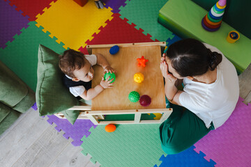 Concentrated boy during SIT classes with educational psychologist holding colored ball for development of sensory sensitivities, top view. Sensory integration therapy