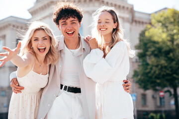 Young three stylish friends posing in the street. Fashion man and two cute female dressed in casual summer clothes. Smiling models having fun. Cheerful women and guy outdoors, in sunny day