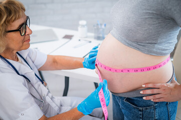 Wall Mural - Doctor measuring the volume of a pregnant woman's abdomen using a tape in inches. 