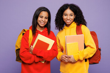 Wall Mural - Two smiling happy fun young teen girl student they wear red yellow casual clothes backpack bag holding books look camera isolated on plain pastel light purple background. High school college concept.