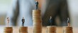 © Thanapipat - representation of income inequality. Small human figures of different genders and ages are standing on stacks of coins of varying heights.