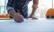 © IBEX.Media - Engineer's hands sketching blueprint with orange pen, hard hats visible, emphasizing safety and precision in construction planning process