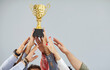 © Studio Romantic - Cropped shot of people hands holding golden trophy cup. Team of joyful employees receiving business award, celebrating great work success. Professional achievement and collaborative success concept.