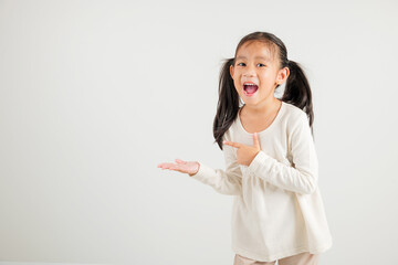 Wall Mural - Asian happy portrait cute young girl smile presenting product holding something on palm away side, studio shot isolated on white background with copy space, kindergarten child show hand gesture