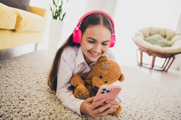 Poster - Full size photo of teen cute girl lying floor headphones device teddy bear wear uniform remote education home schooling indoors background