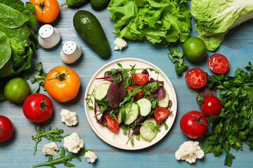 Wall Mural - Healthy vegetarian food. Plate of salad and vegetables on light blue wooden table, flat lay