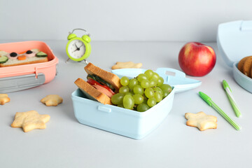 Lunch box with snacks, alarm clock and stationery on white table