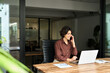 © insta_photos - Busy happy young woman manager talking on phone in office. Professional lady entrepreneur, business woman client manager making business call on cellphone at work communicating using laptop in office.