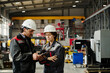 © TrueFrame Collective - Engineers wearing safety helmets collaborating on project in industrial workshop with various machinery in background