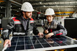 © TrueFrame Collective - Engineers in hard hats examining solar panel in industrial environment, discussing installation process