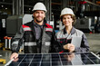 © TrueFrame Collective - Engineers wearing hard hats and safety jackets standing next to a solar panel, smiling in industrial factory