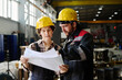 © TrueFrame Collective - Two construction workers reviewing project blueprints inside large industrial facility