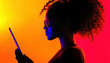 © Narongsak - A captivating silhouette of a person with curly hair, wearing sunglasses, engaging with a tablet against a striking gradient backdrop of orange and red hues.