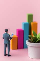 Poster - Businessman analyzing colorful bar graph with plant on pink background, symbolizing growth and progress in a modern and vibrant setting.