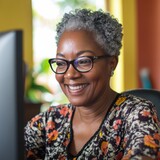 mature older eldery black African American woman around her computer focused and happy as she focuses on the computer screen 