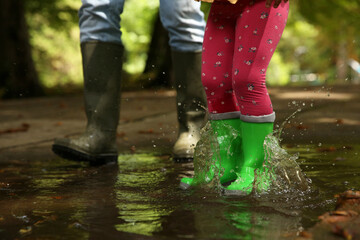 Mother and daughter wearing rubber boots standing in puddle outdoors, closeup