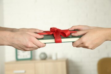 Wall Mural - Woman gifting her friend book tied with red ribbon indoors, closeup