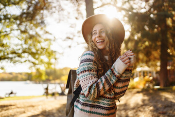 A joyful woman in a patterned sweater and hat enjoying a sunny autumn day in a vibrant forest. Travel, tourism, weekend.