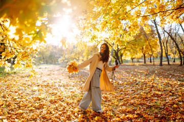 A joyful woman enjoying a sunny autumn day in a park, surrounded by vibrant yellow leaves and a serene atmosphere. Leisure activity.